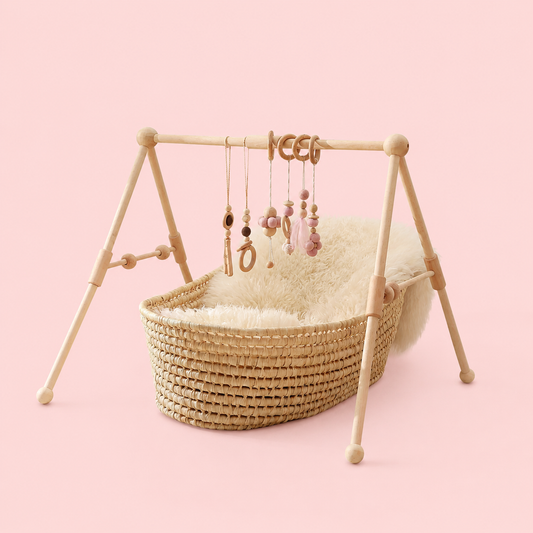 Wicker baby crib with wooden stand and hanging toys on a pink background