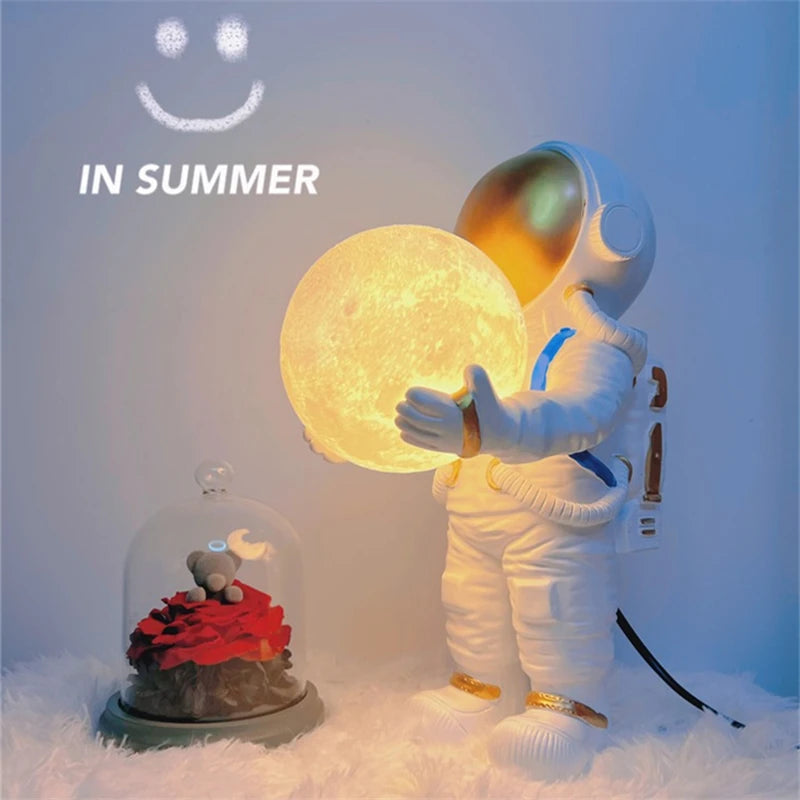 Astronaut holding a moon-shaped lamp with 'IN SUMMER' text above, on a snowy background.