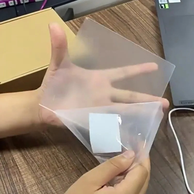 Hand holding a clear plastic sheet over a white square on a wooden surface.