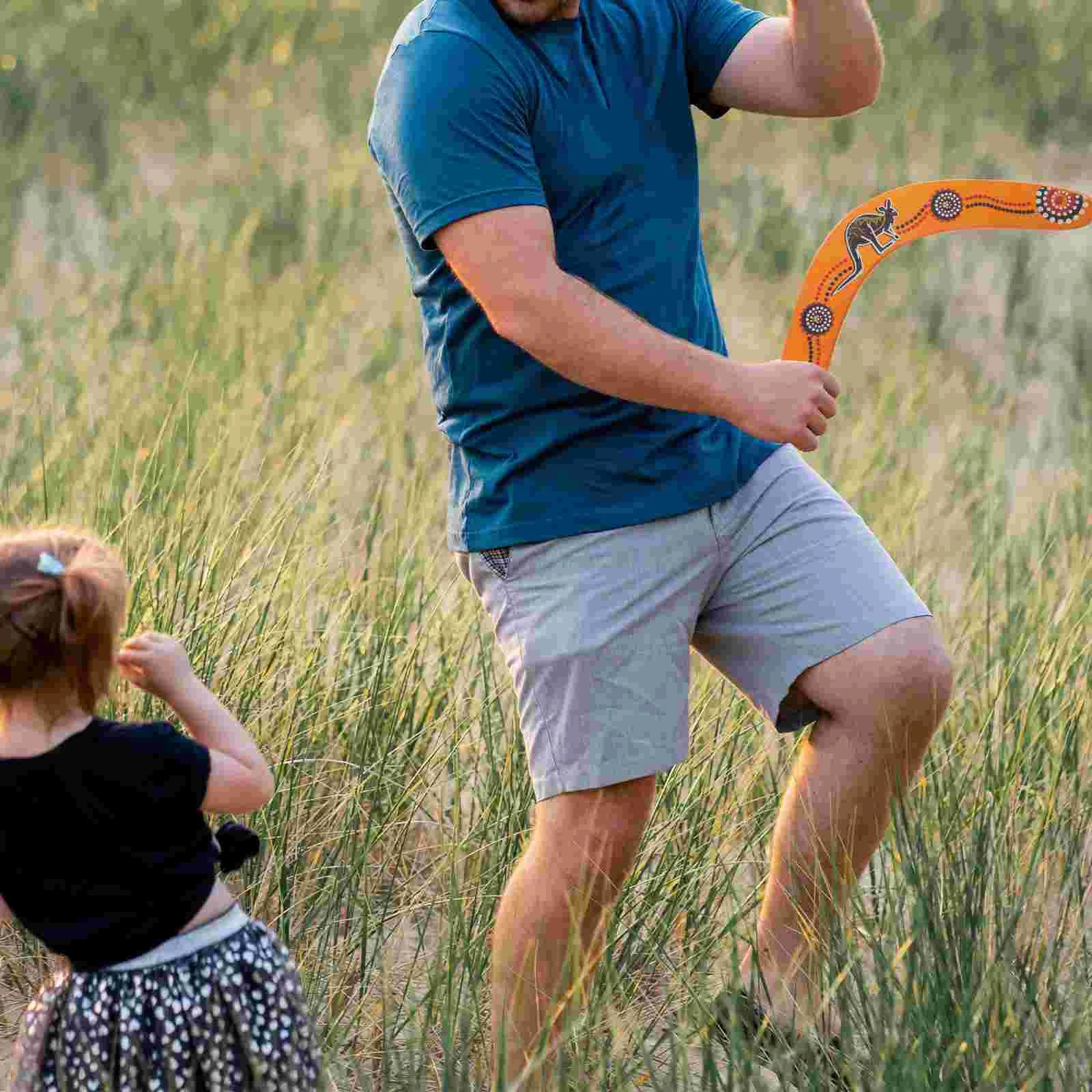 Man playing with Decorative boomerang with Aboriginal art design held by a hand with a child watching.