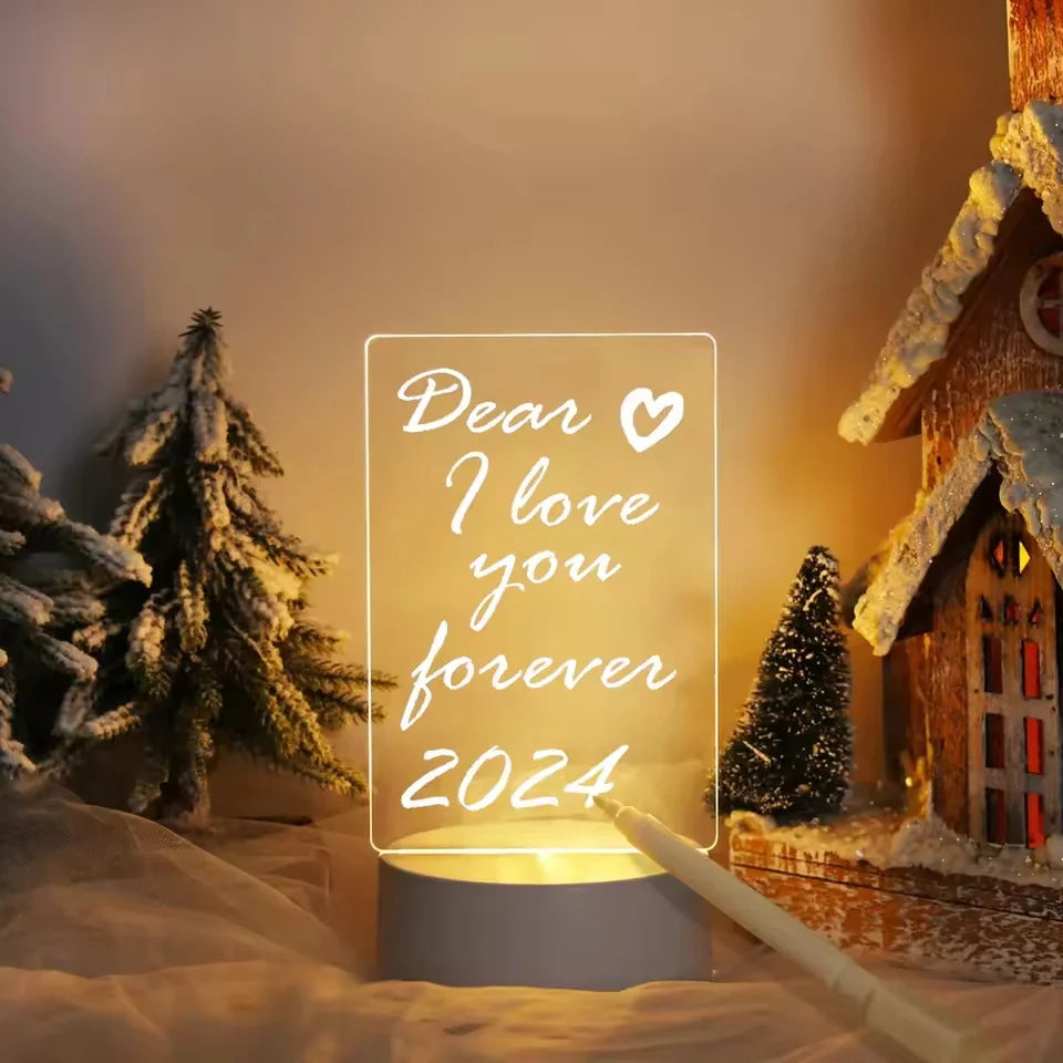 Glowing sign with 'Dear I love you forever 2024' text in a snowy landscape with a cabin and trees.