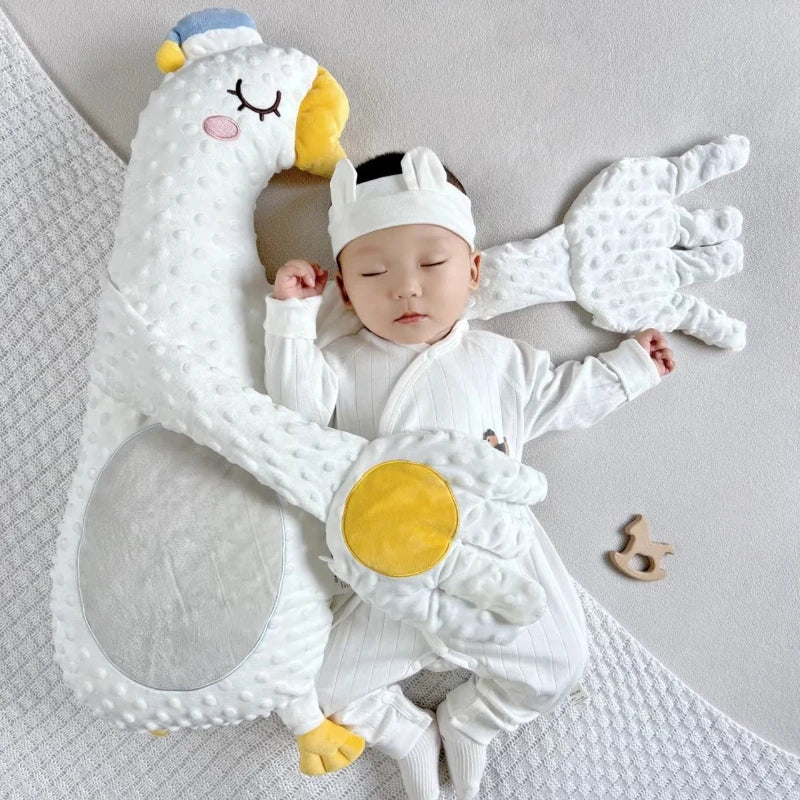 Baby in a swan costume lying on a soft surface with a swan-shaped pillow.