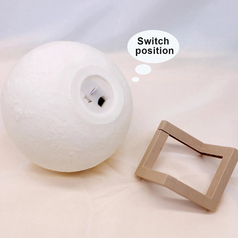 Moon-shaped lamp on a stand with a cardboard square on a light gray background