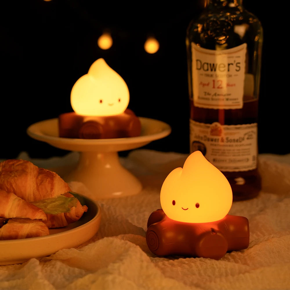 Two small flame-shaped lights on a table with a bottle of Dower's whiskey and pastries.