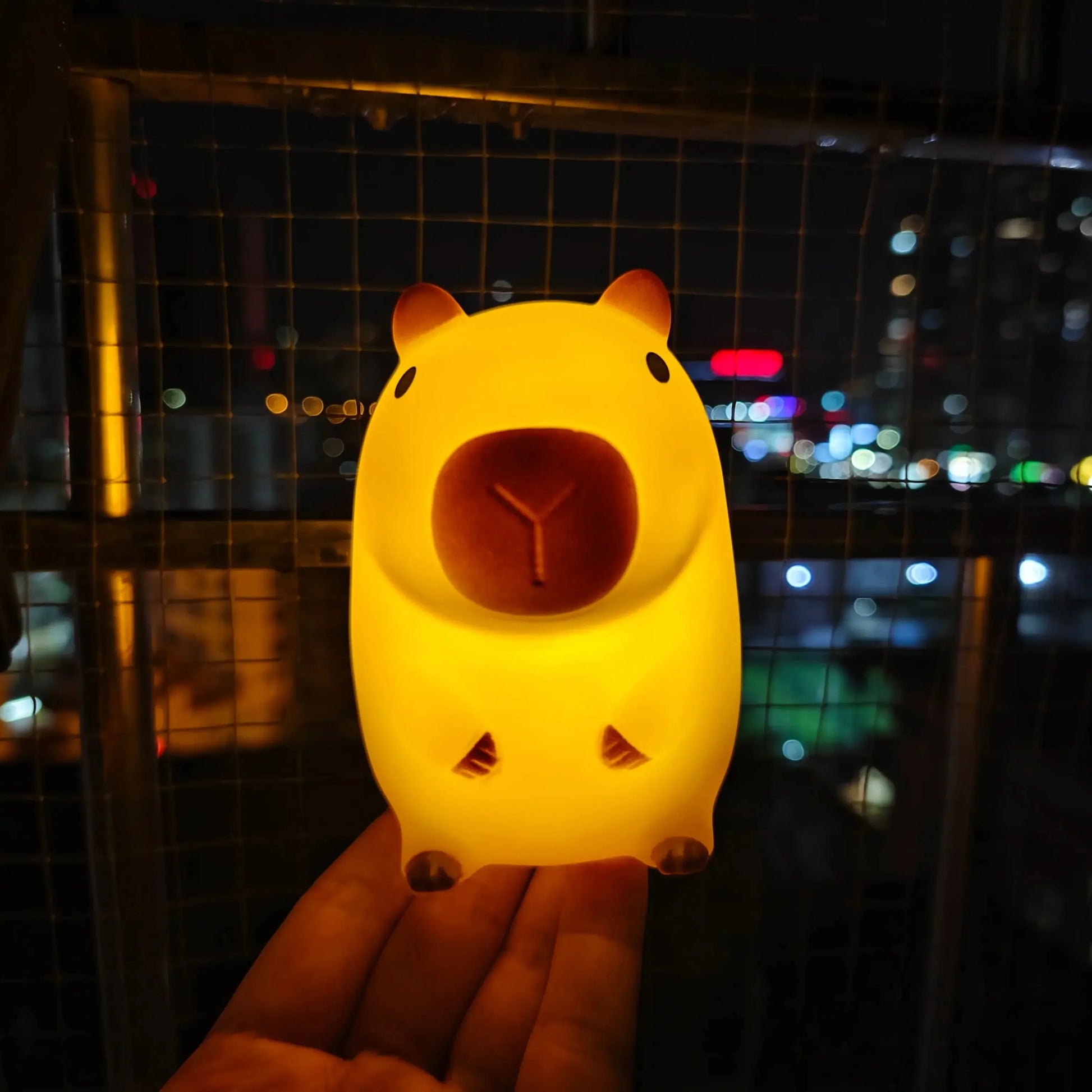 Hand holding a Cute Capybara-shaped night light with a cityscape in the background